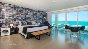 Une chambre d’hôtel moderne avec un grand lit, une banquette, un bureau et une vue sur l’océan.