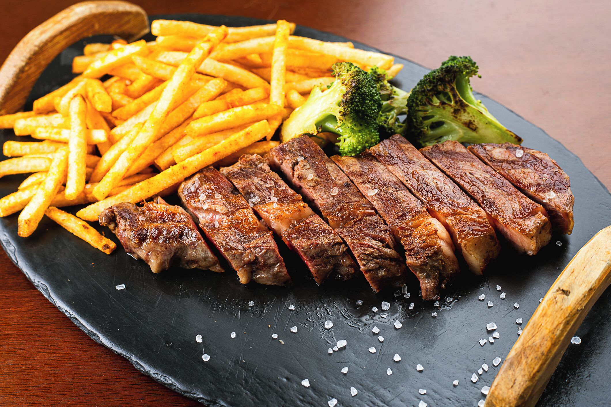 A plate of steak, fries, and broccoli on a slate serving board.