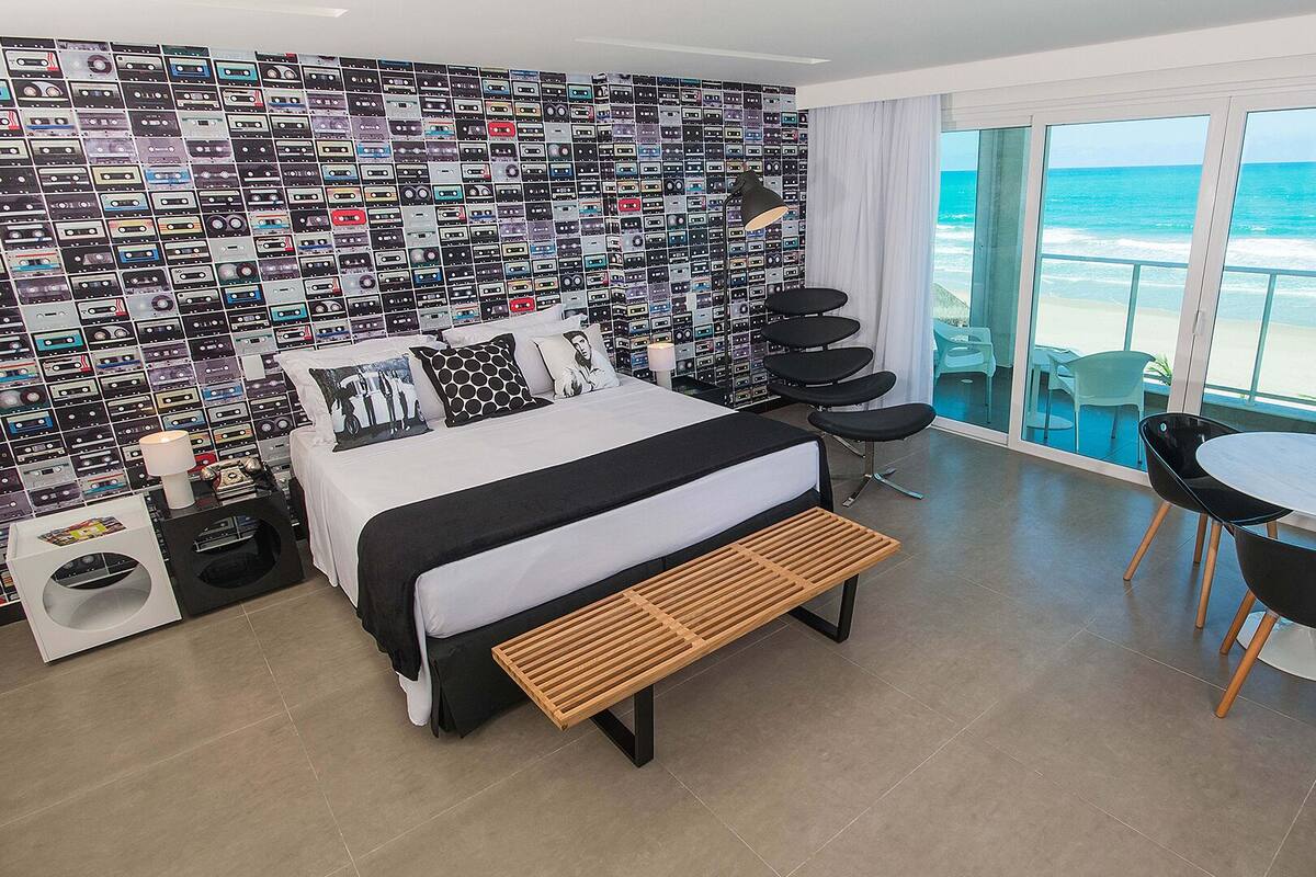 Ein modernes Hotelzimmer mit Bett, einer Bank, einem Tisch und Blick auf den Ozean.