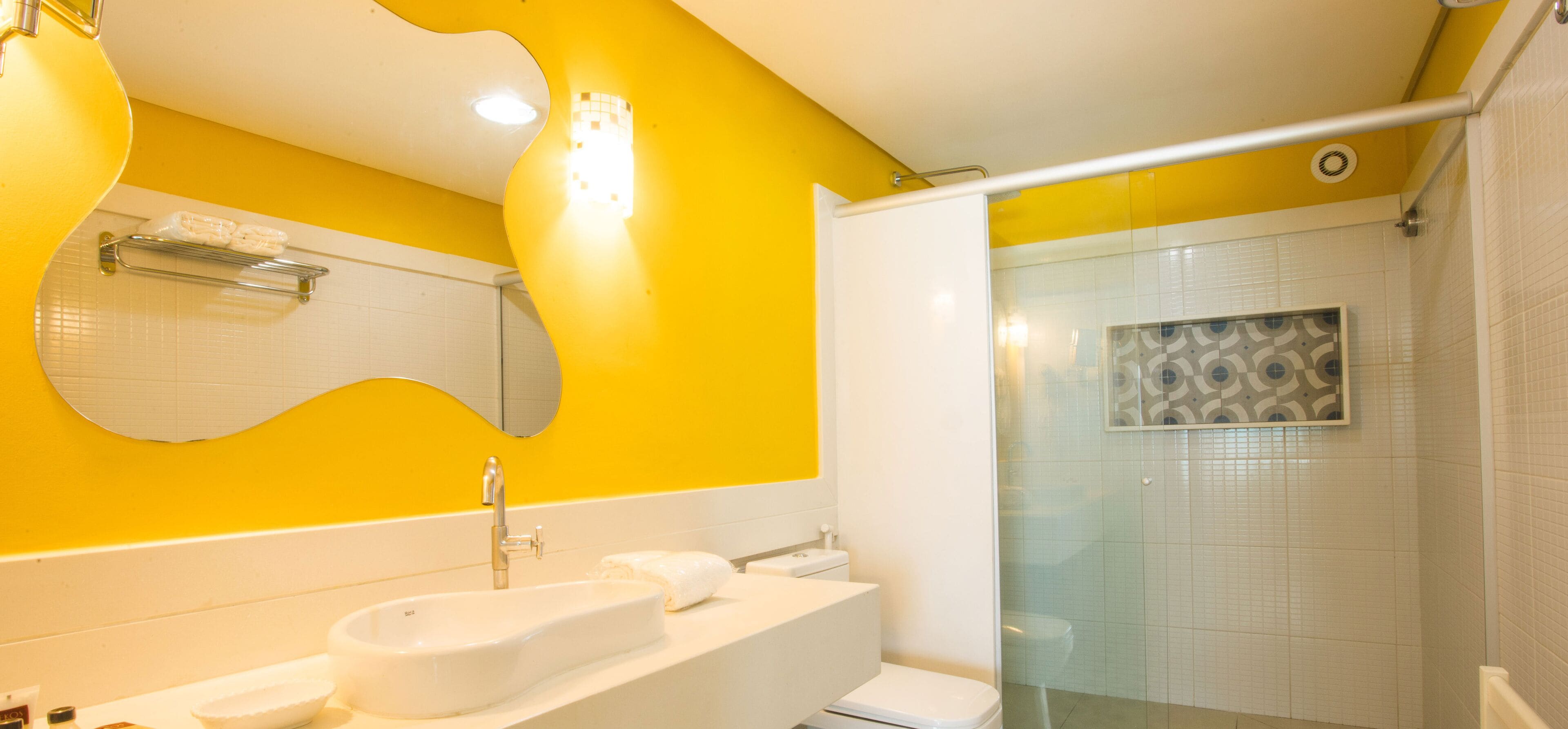 Un baño con una pared amarilla, un lavabo blanco, un espejo y una zona de ducha.