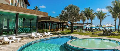 A pool area with lounge chairs, a glass-enclosed building, and palm trees.