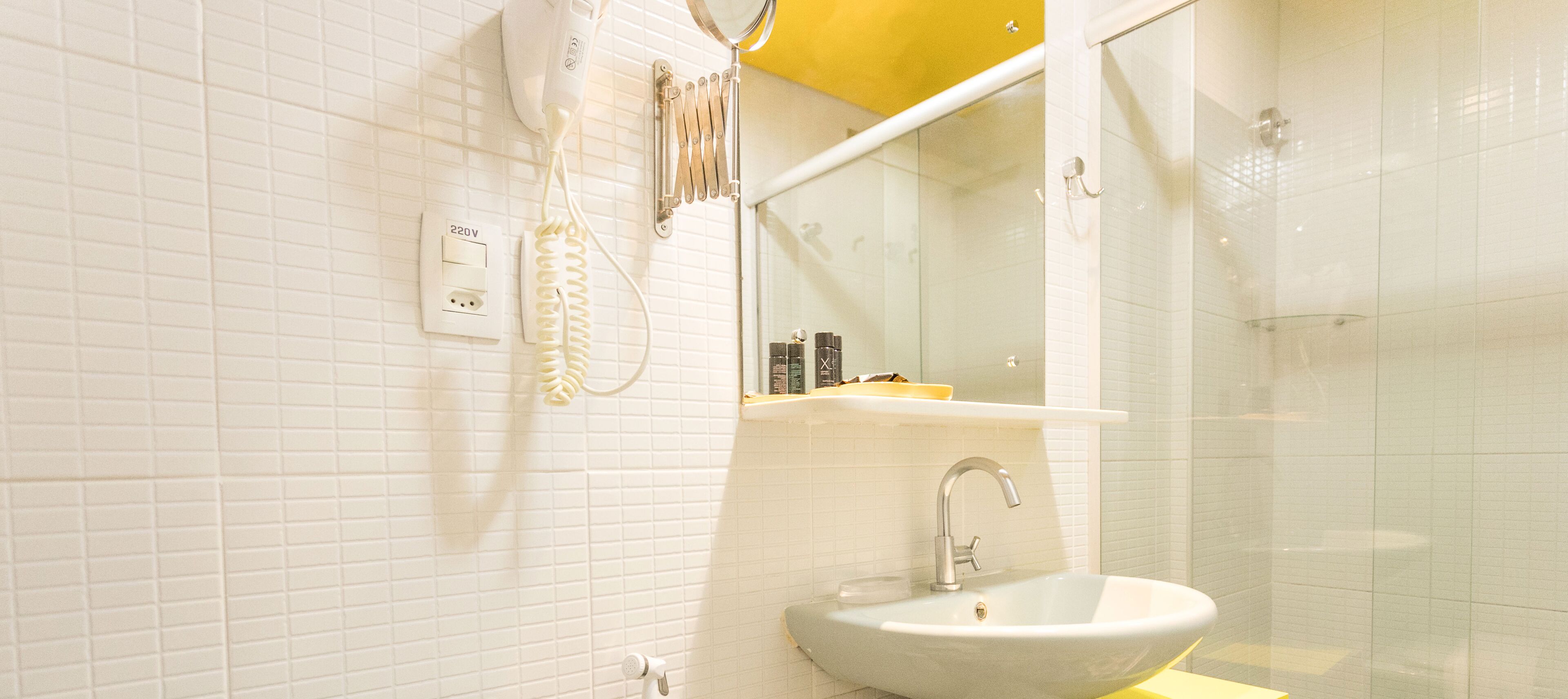 A bathroom with a white sink, a mirror, a towel rack, and a shower enclosure.