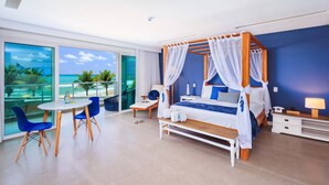 Une chambre moderne avec un lit à baldaquin, un balcon offrant une vue sur la mer et un coin salon avec des chaises bleues.