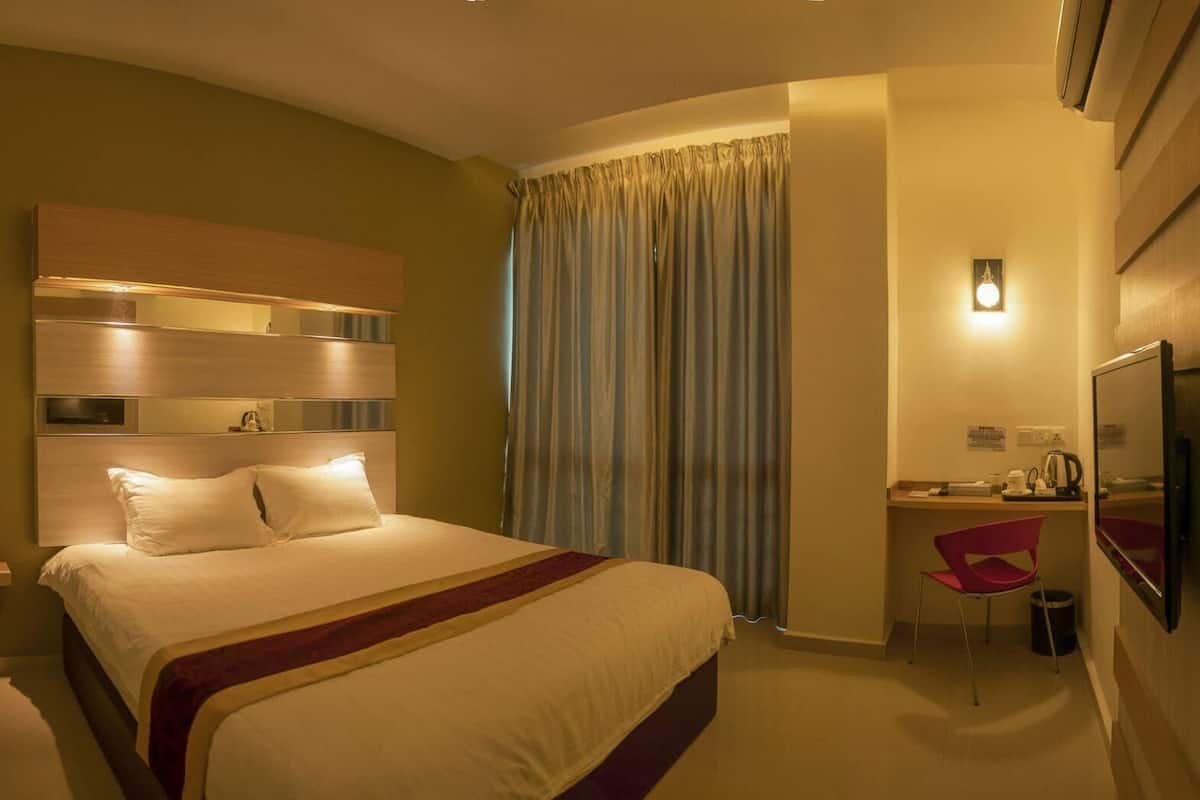 A hotel room with a bed, a desk, a chair, a TV, and a window with curtains.