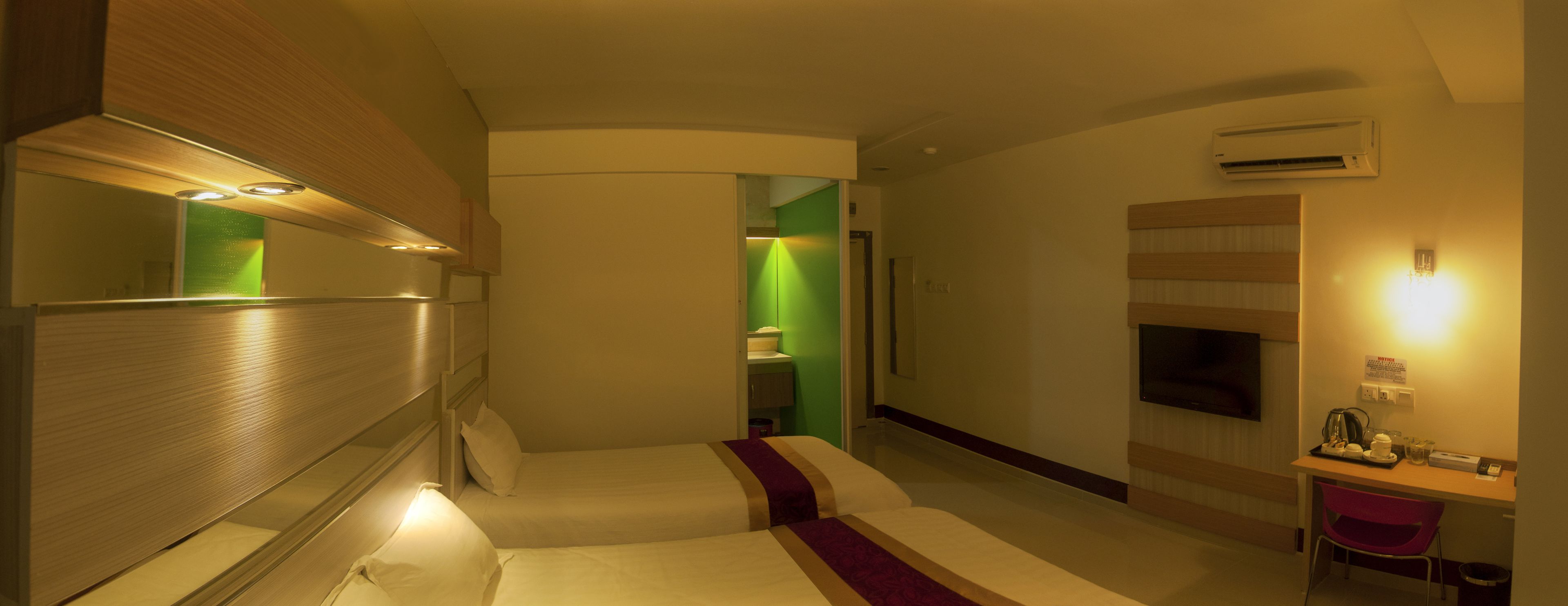 A hotel room with a bed, a desk with a chair, a television, and an air conditioning unit.