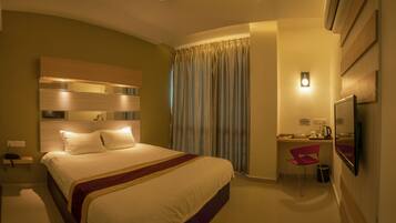 Una habitación de hotel con cama, escritorio, silla, televisor y cortina.
