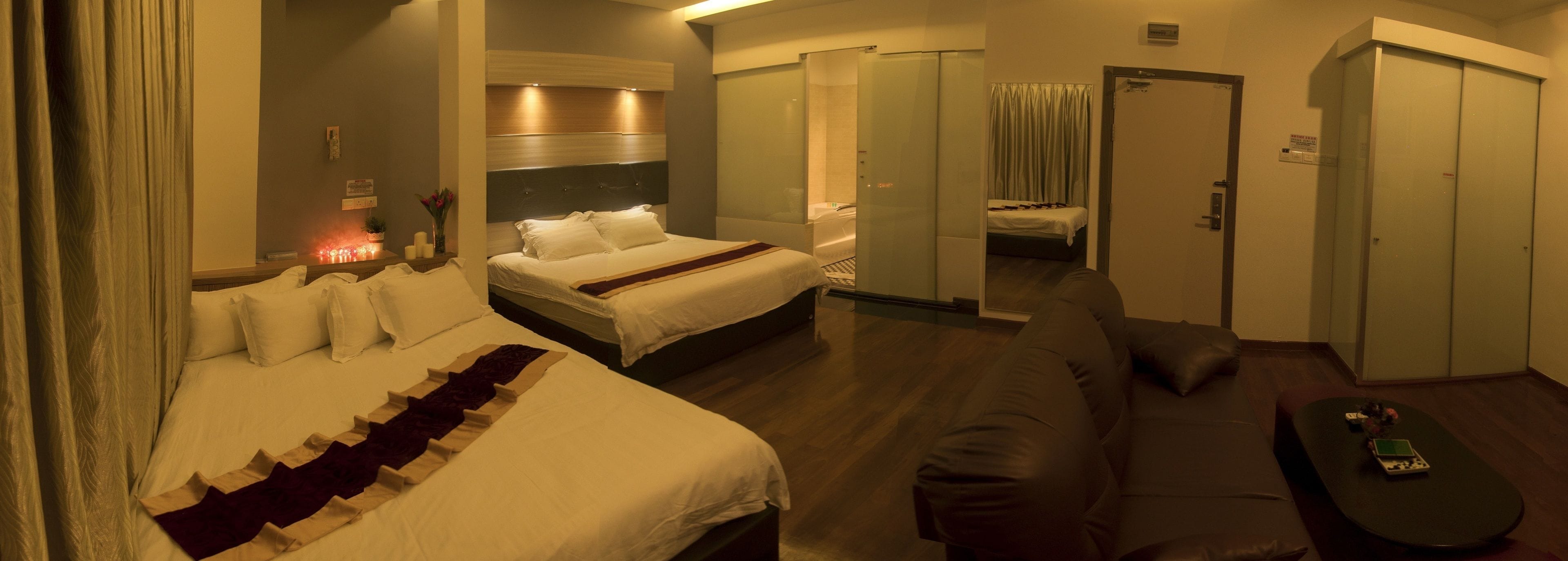 A hotel room with a large bed, a smaller bed, a sofa, and a table. There are curtains, a mirror, and a sign on the wall.