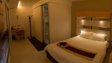 A hotel room with a bed, a coat rack, a shower, and a small table with a chair.