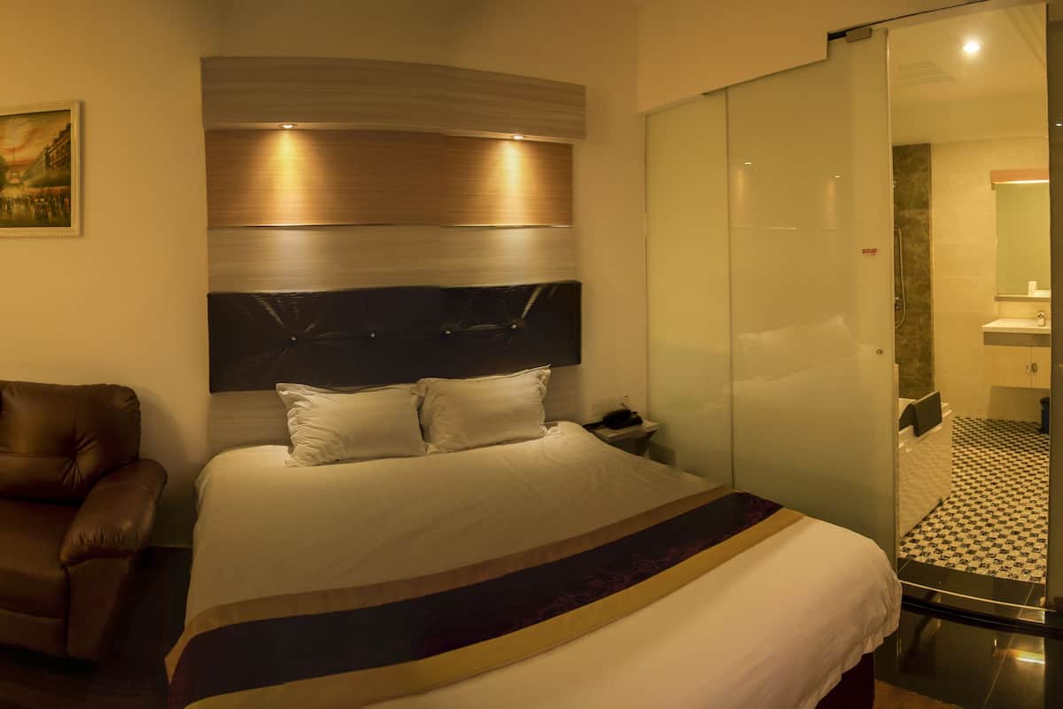 A hotel room with a large bed, a desk with a chair, a leather armchair, and a small round table.