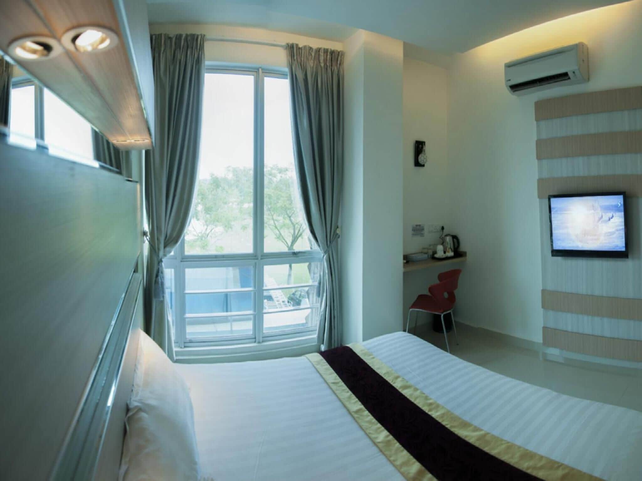 A hotel room with a bed, a desk with a chair, a television, and a window with curtains.