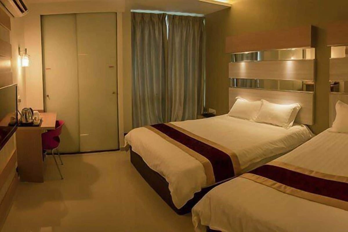 Quarto de hotel com duas camas, uma escrivaninha, uma cadeira e um guarda-roupa.