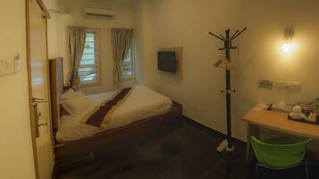 A hotel room with a bed, a desk with a chair, a coat rack, and a wall-mounted light.