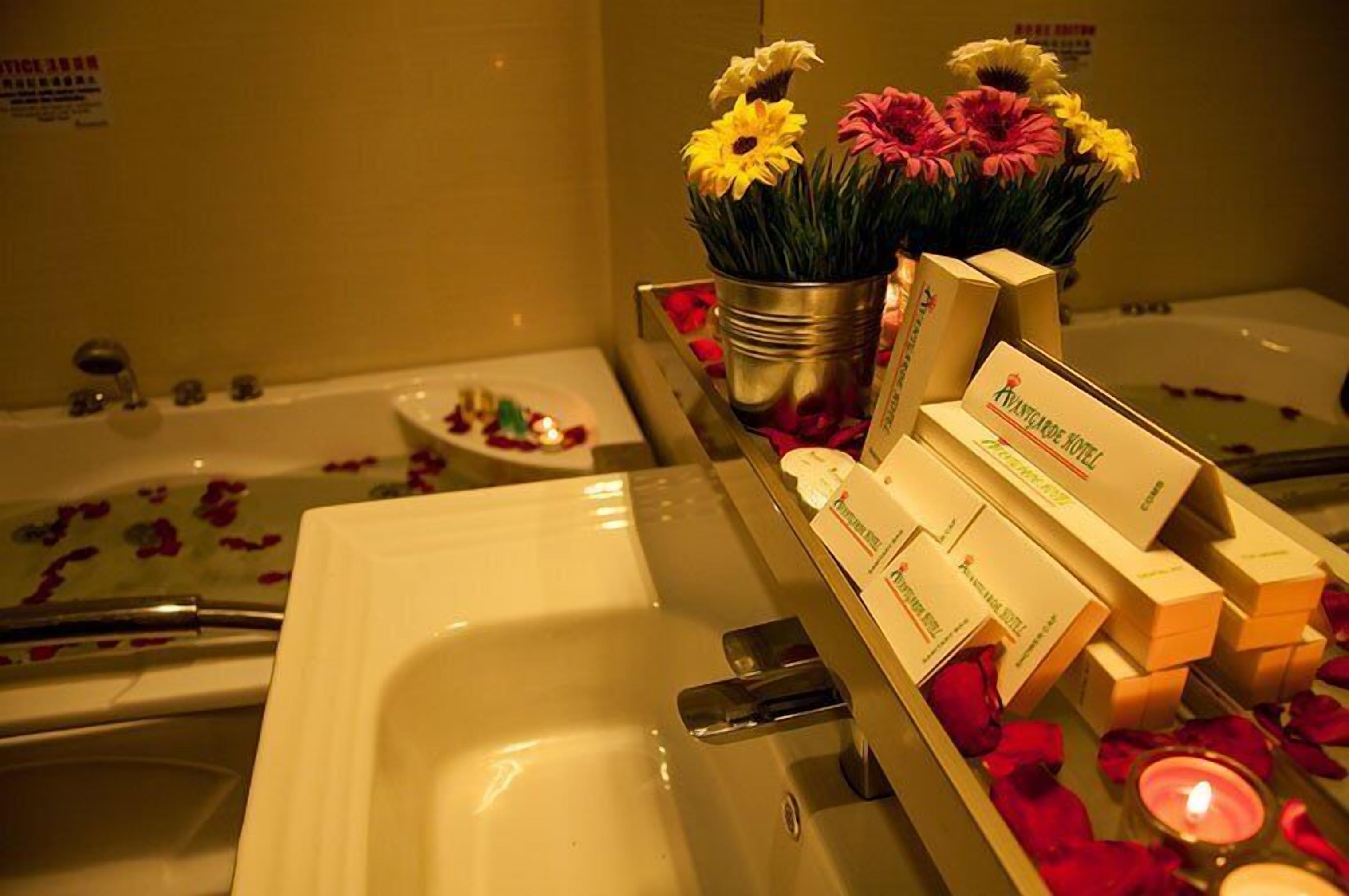 A hotel bathroom with a bathtub, a sink, and a mirror. There are rose petals and a candle on the counter.