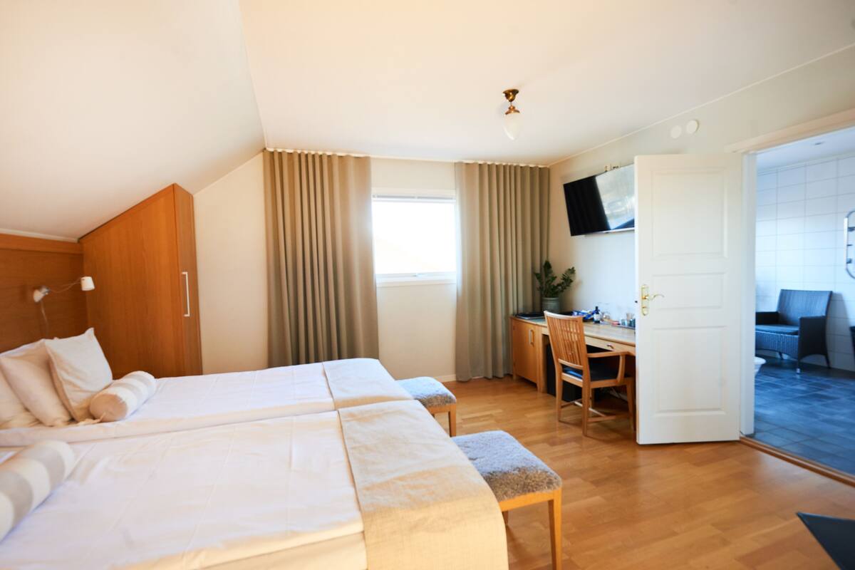 Une chambre d’hôtel avec deux lits, un bureau, une chaise, une télévision et une porte donnant sur un balcon.