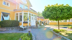 Un bâtiment jaune avec un porche abrité, un banc et un arbre au premier plan.