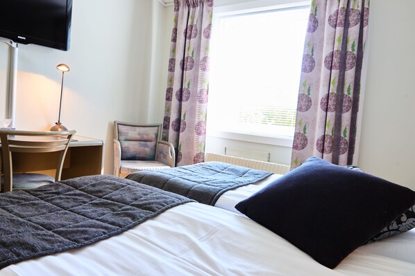 A hotel room with two beds, a desk, a chair, a television, and curtains.