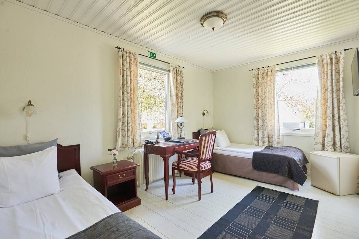 Une pièce comprenant un lit, un bureau, une chaise et un canapé. Il y a une fenêtre avec des rideaux, un radiateur et une lampe sur le bureau.