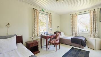 A room with a bed, a desk, a chair, and a sofa. There is a window with curtains, a radiator, and a lamp on the desk.