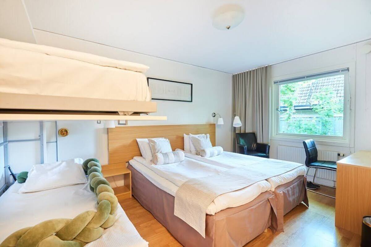 Une chambre d’hôtel avec un grand lit, un bureau, une chaise et une fenêtre donnant sur un paysage verdoyant.
