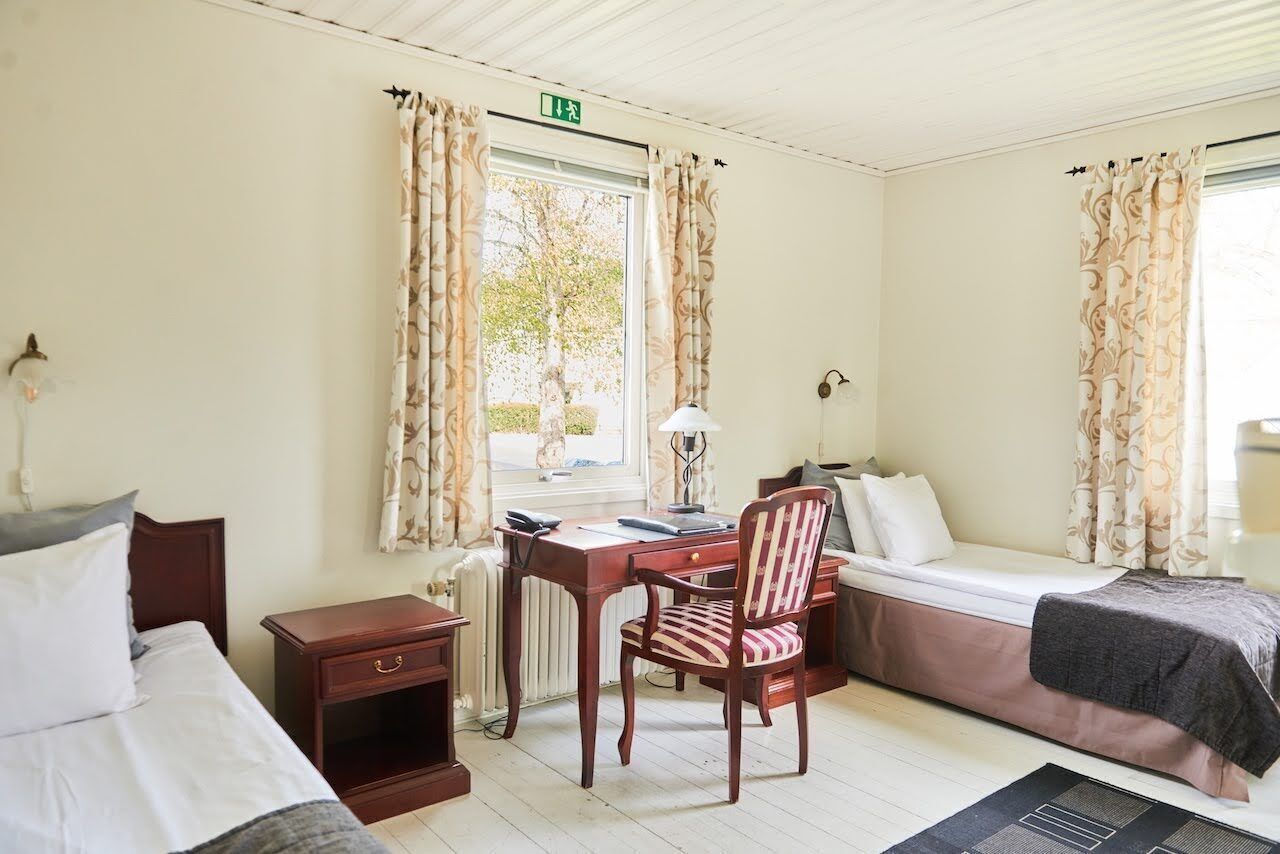 Una habitación con cama, escritorio, silla y ventana con cortinas.