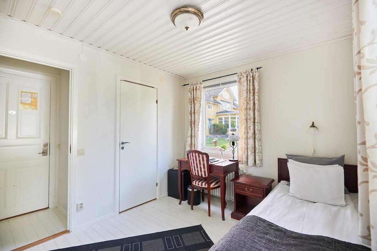 Une pièce comprenant un lit, un bureau avec une chaise, une fenêtre avec des rideaux et une porte.