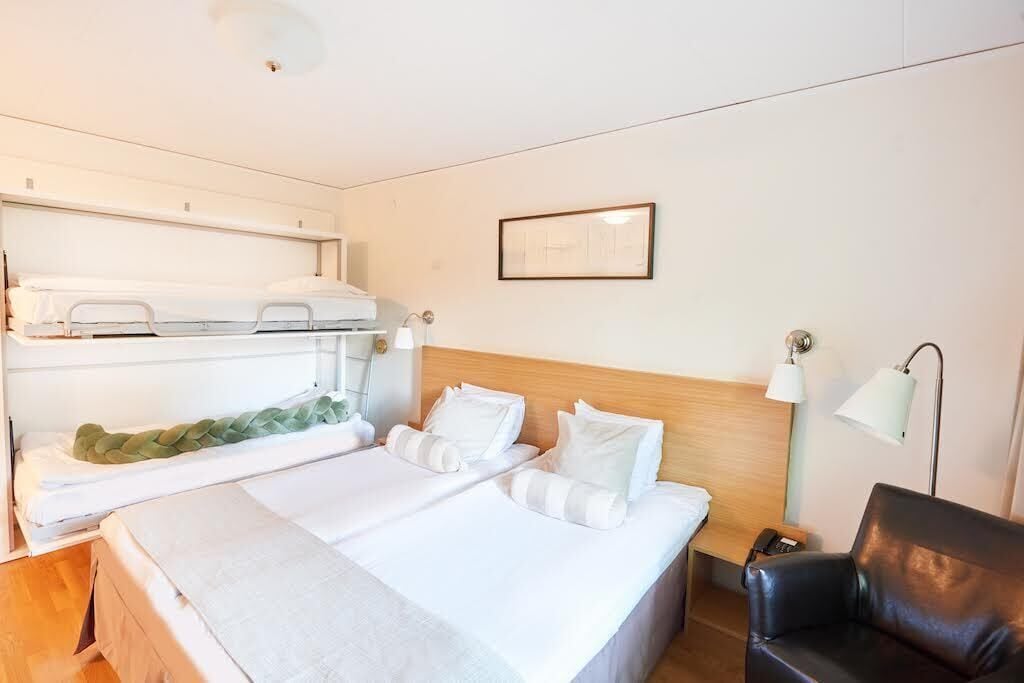Une chambre d’hôtel avec deux lits, une tête de lit en bois, un bureau avec une lampe, une chaise et un tableau encadré au mur.