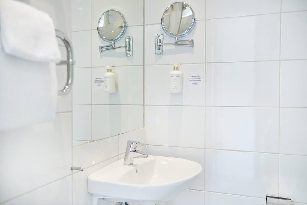Une salle de bain moderne avec un lavabo blanc, deux miroirs fixés au mur et deux flacons de produits de toilette.