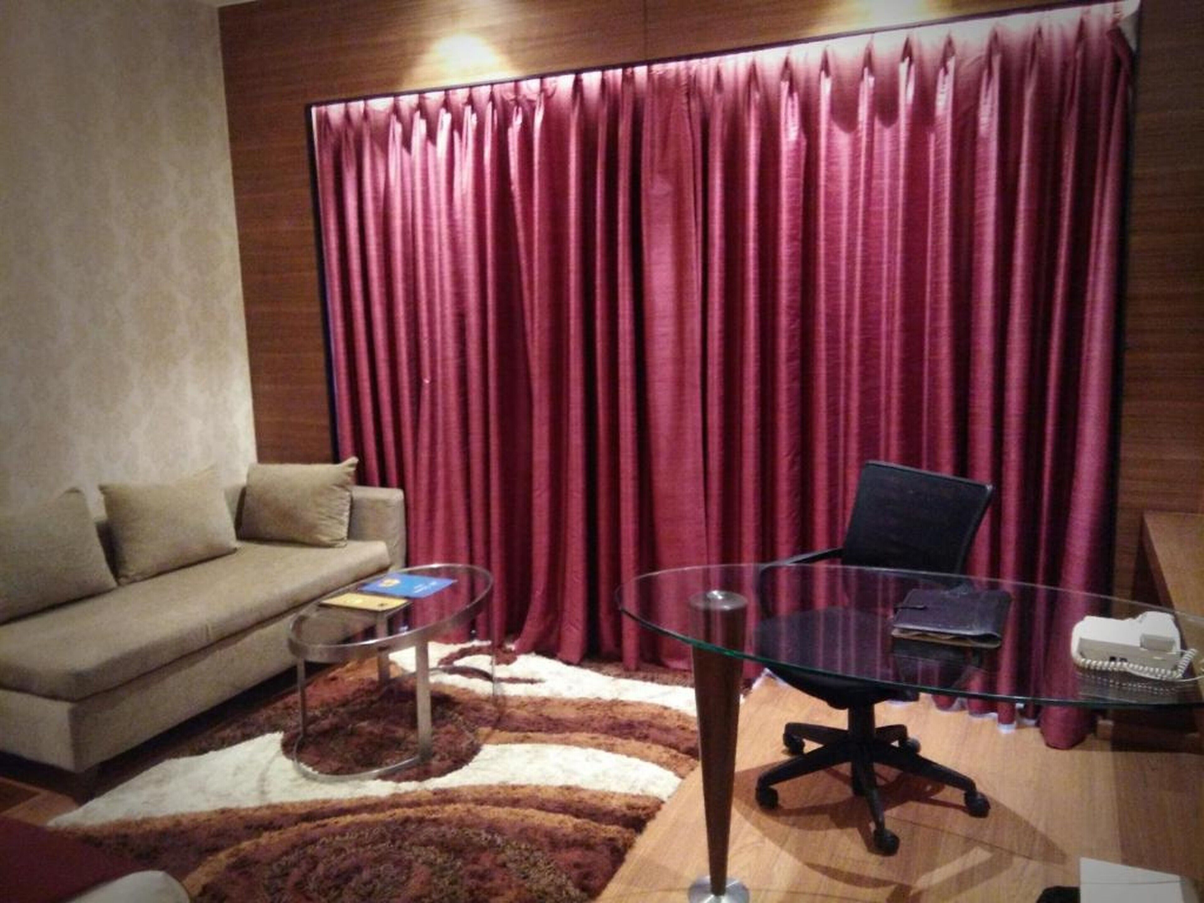 A room with a sofa, a glass table, a chair, a rug, and a curtain.