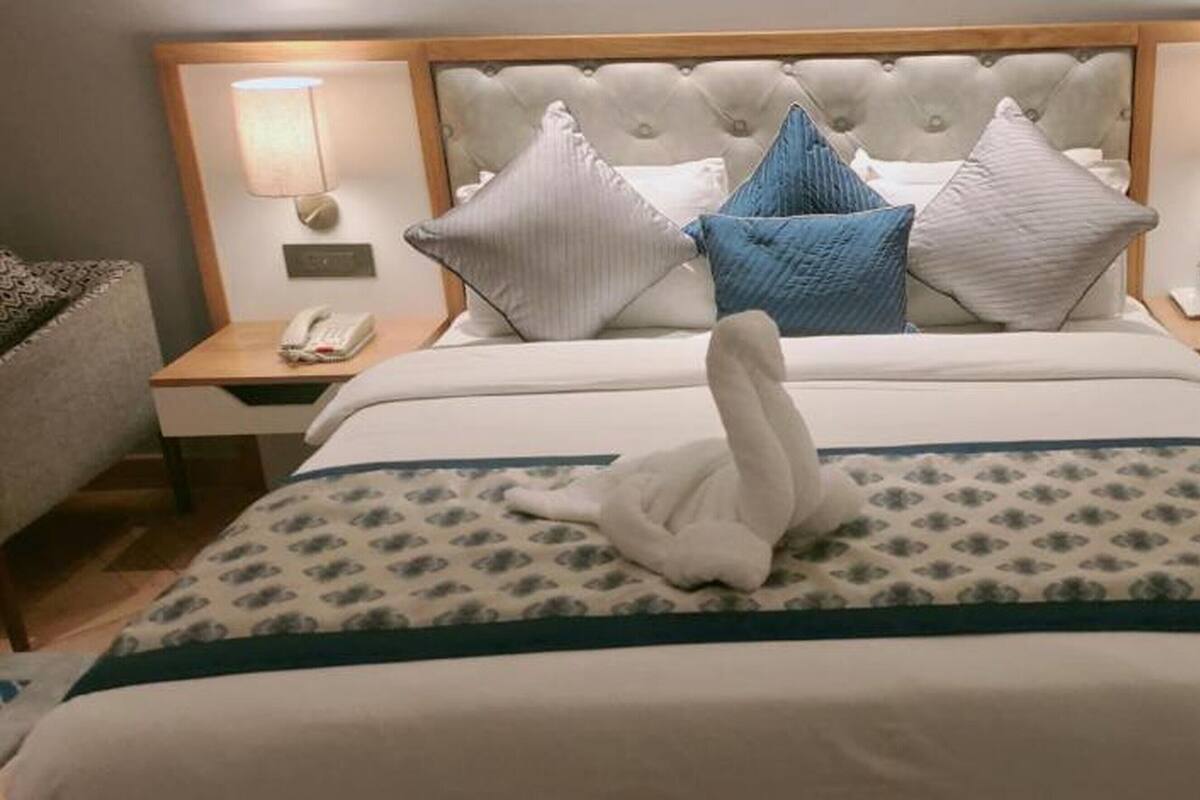 A hotel room with a large bed, a headboard with a tufted design, two bedside tables with lamps, and a swan-shaped pillow.