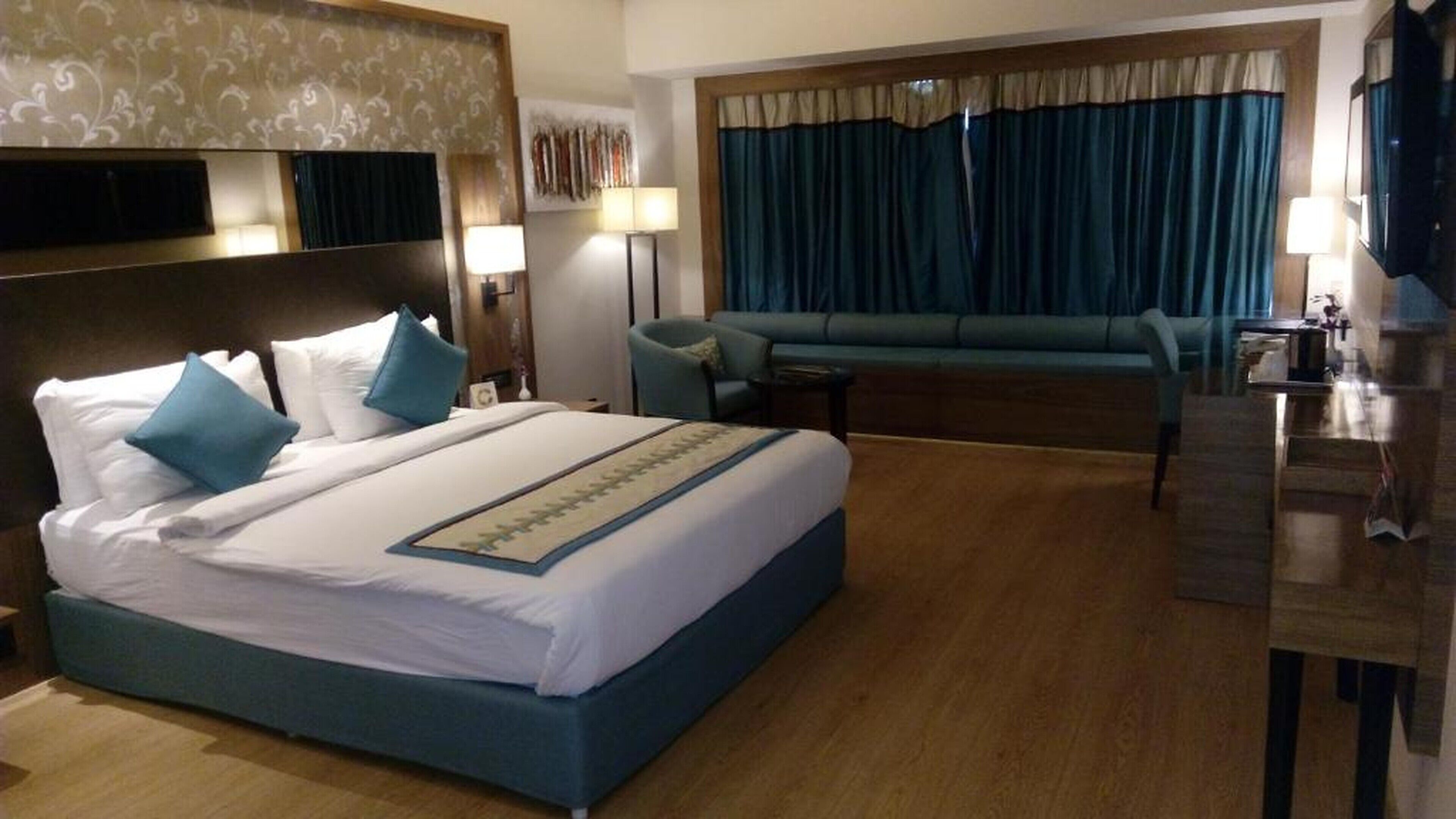 A hotel room with a large bed, a sofa, a desk, and a TV.