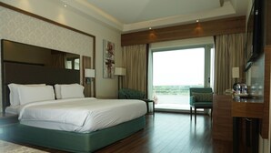 A hotel room with a large bed, a desk, a chair, and a balcony with a view. - VW Canyon (Raipur)