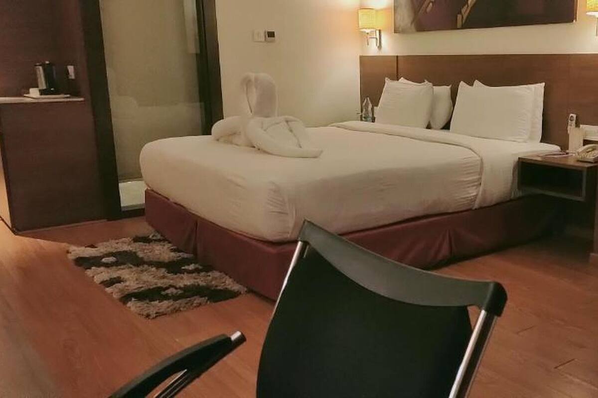 A hotel room with a bed, a chair, a small table, and a nightstand with a lamp.
