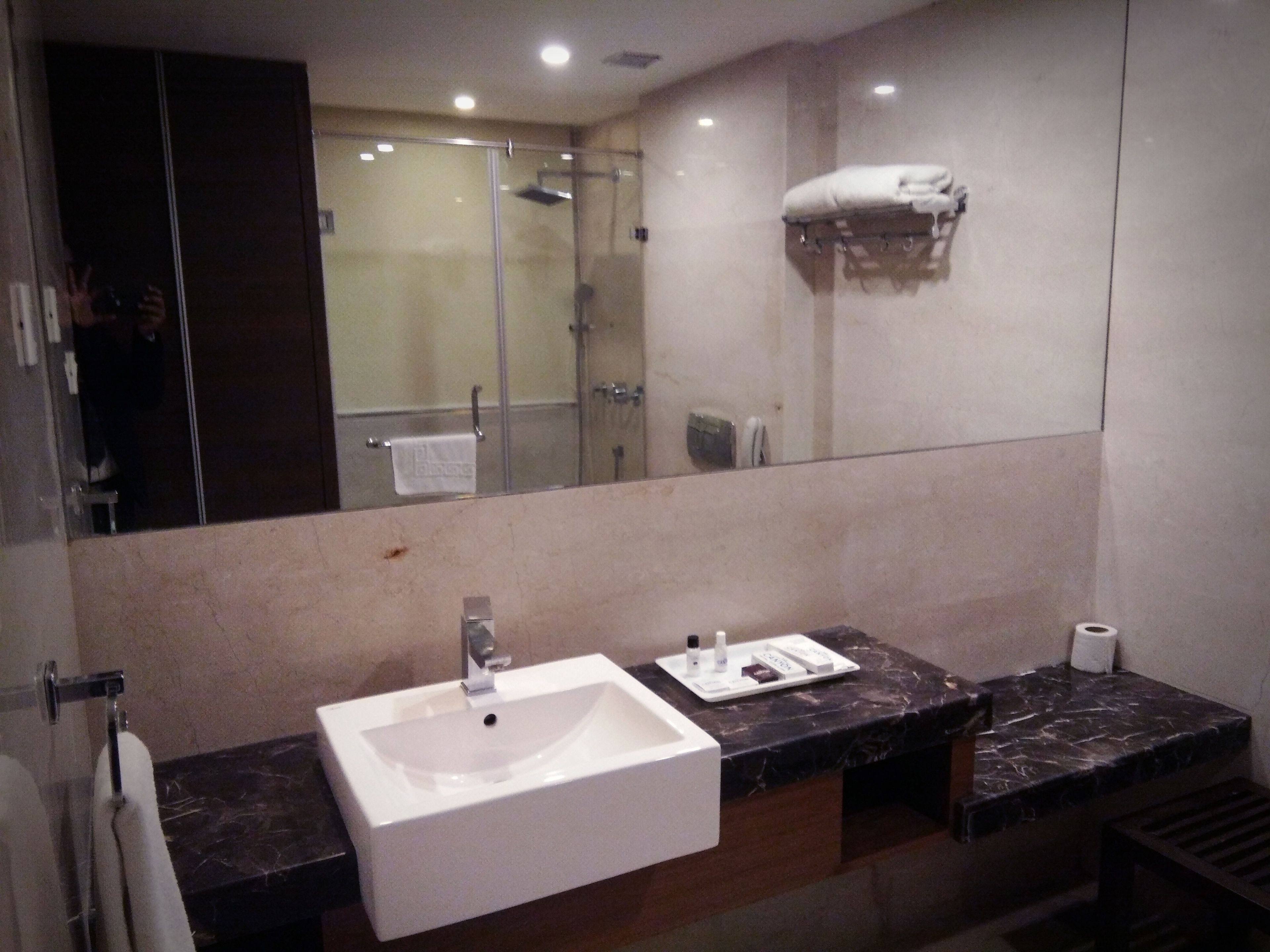 A modern bathroom with a large mirror, a white sink, and a marble countertop.
