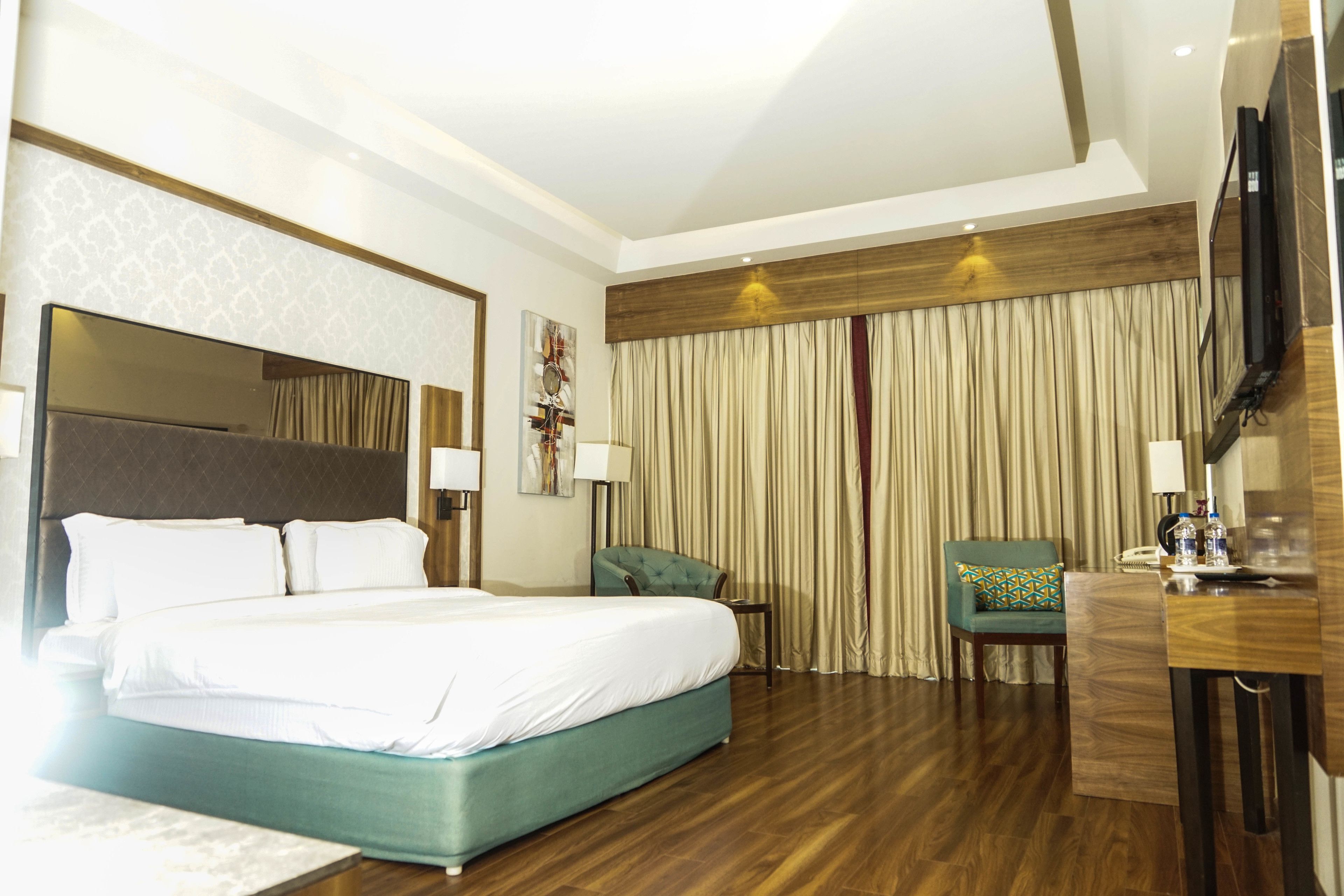 A hotel room with a large bed, a desk with a chair, a TV, and a curtain.
