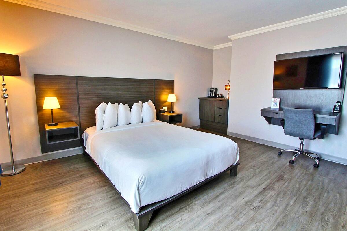 A hotel room with a large bed, bedside lamps, a desk with a chair, a flat-screen TV, and a minibar.