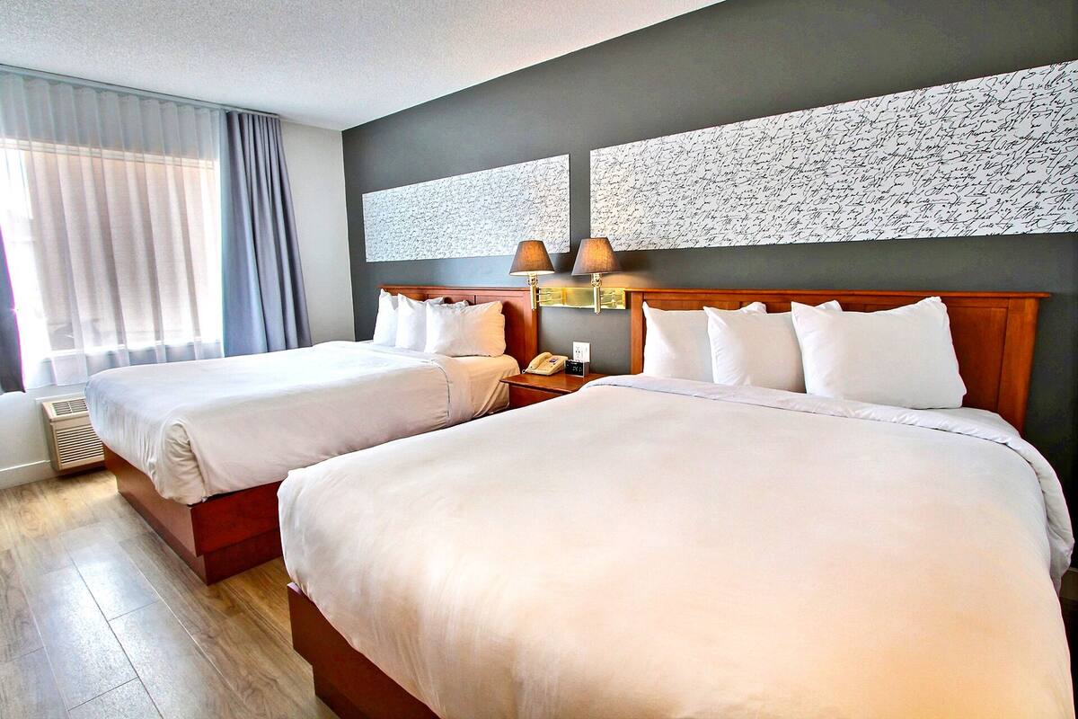A hotel room with two beds, a nightstand with a lamp, a telephone, and a wall with a textured pattern.