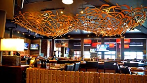 A restaurant with a modern interior, featuring a unique ceiling design, brick walls, and multiple TV screens. - Hôtel L'Empress (Rimouski)