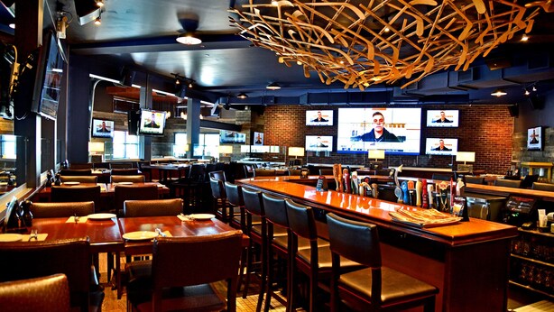 A restaurant with multiple TV screens, wooden bar counter, and leather seating. - Hôtel L'Empress (Rimouski)