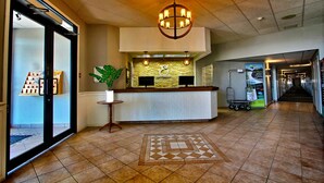 A hotel reception area with a tiled floor, a reception desk, a large chandelier, and a potted plant. - Hôtel L'Empress (Rimouski)