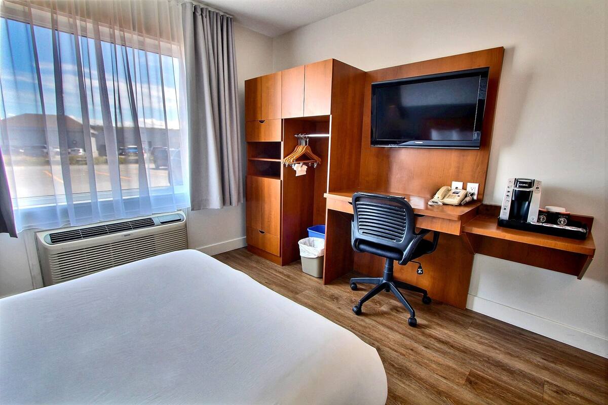 A hotel room with a bed, a desk with a chair, a TV, a telephone, and a coffee maker.