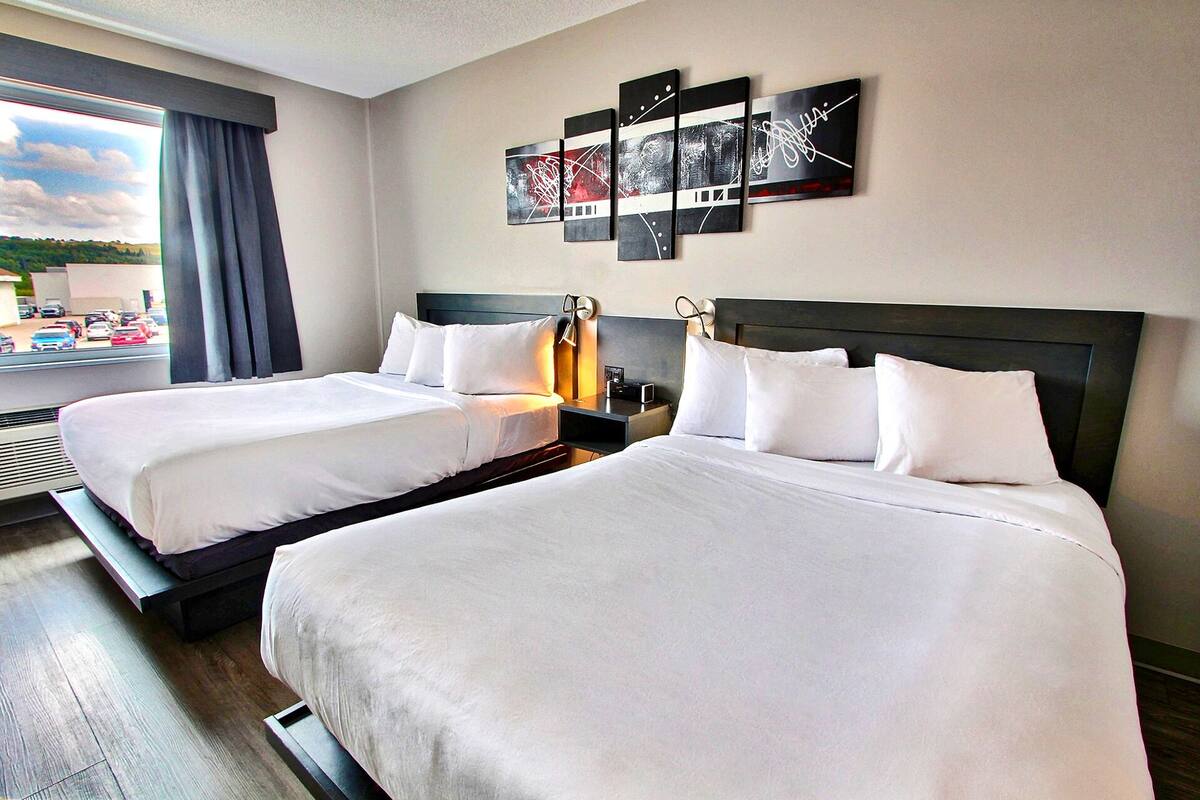 A hotel room with two beds, a large window with a view, and a wall art piece above the beds.