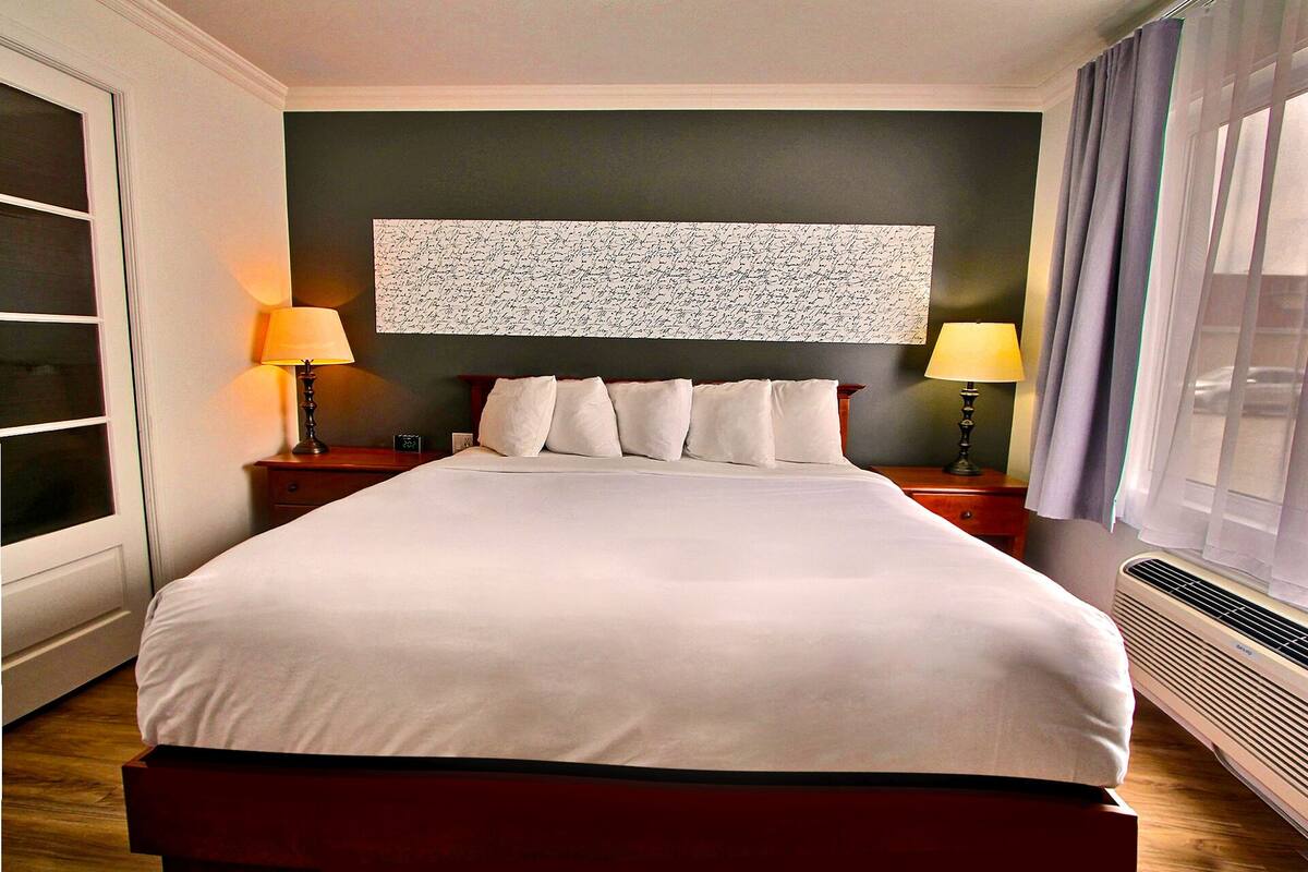 A hotel room with a large bed, two bedside tables with lamps, a wall-mounted artwork, and a window with curtains.