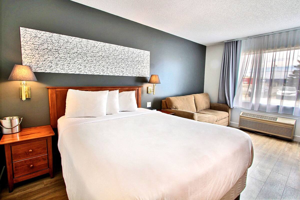 A hotel room with a large bed, two bedside lamps, a sofa, a wall-mounted artwork, and a window with curtains.
