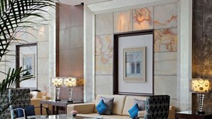 A modern lobby with marble walls, a sofa with blue cushions, and two floor lamps. - SK Premium Park (New Delhi)