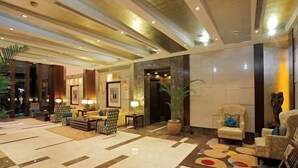 A lobby with a patterned carpet, seating area with armchairs and tables, and a large potted plant. - SK Premium Park (New Delhi)