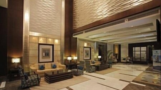 A spacious lobby with a high ceiling, a central seating area with sofas and armchairs, a patterned floor, and framed artwork on the walls. - SK Premium Park (New Delhi)