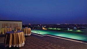A rooftop pool area with tables and chairs, overlooking a cityscape at night. - SK Premium Park (New Delhi)