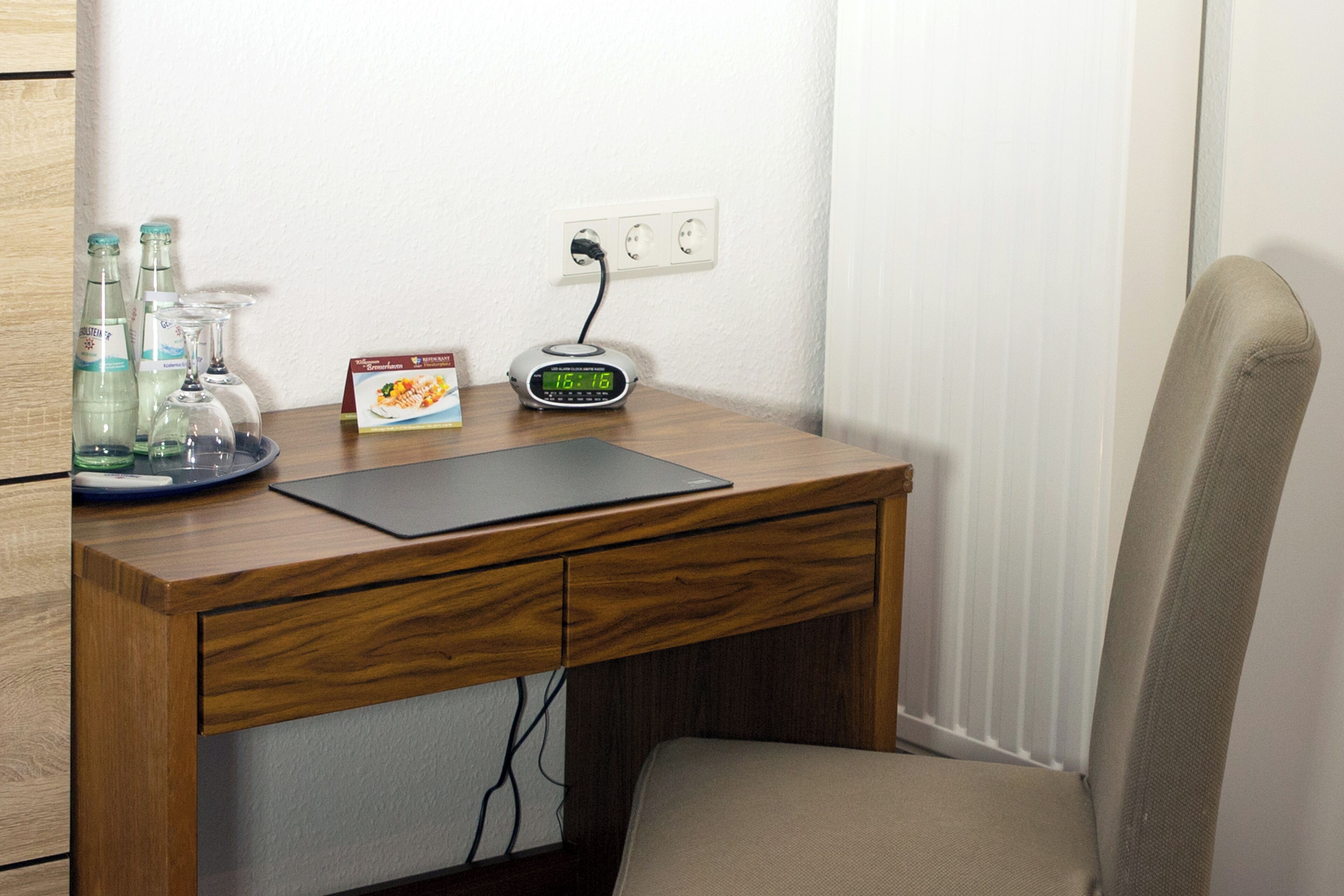 Escritorio de madera con una computadora portátil, un reloj digital y un plato de vidrio con botellas y una caja.