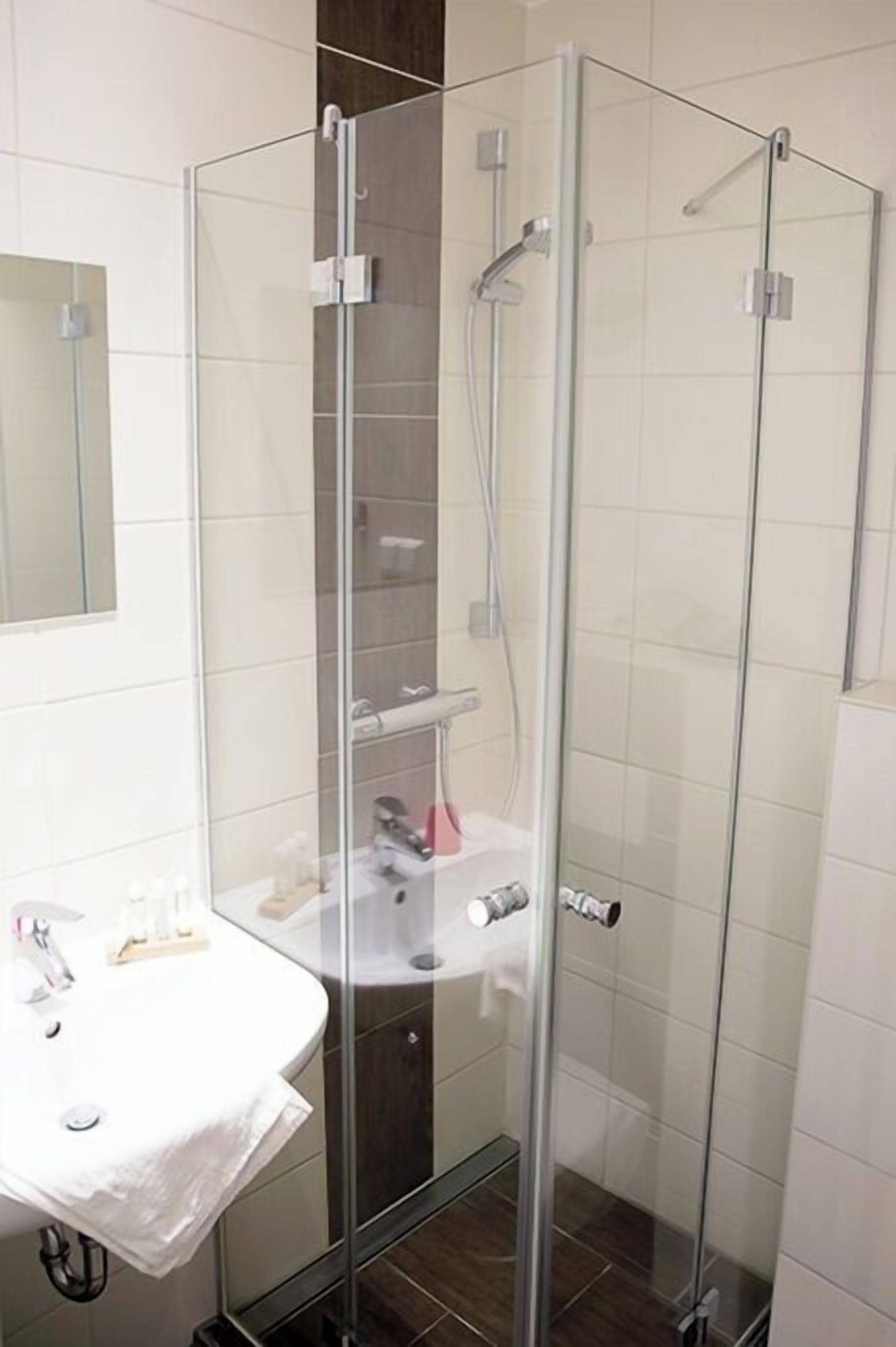 Un baño moderno con ducha acristalada, lavamanos blanco y espejo.