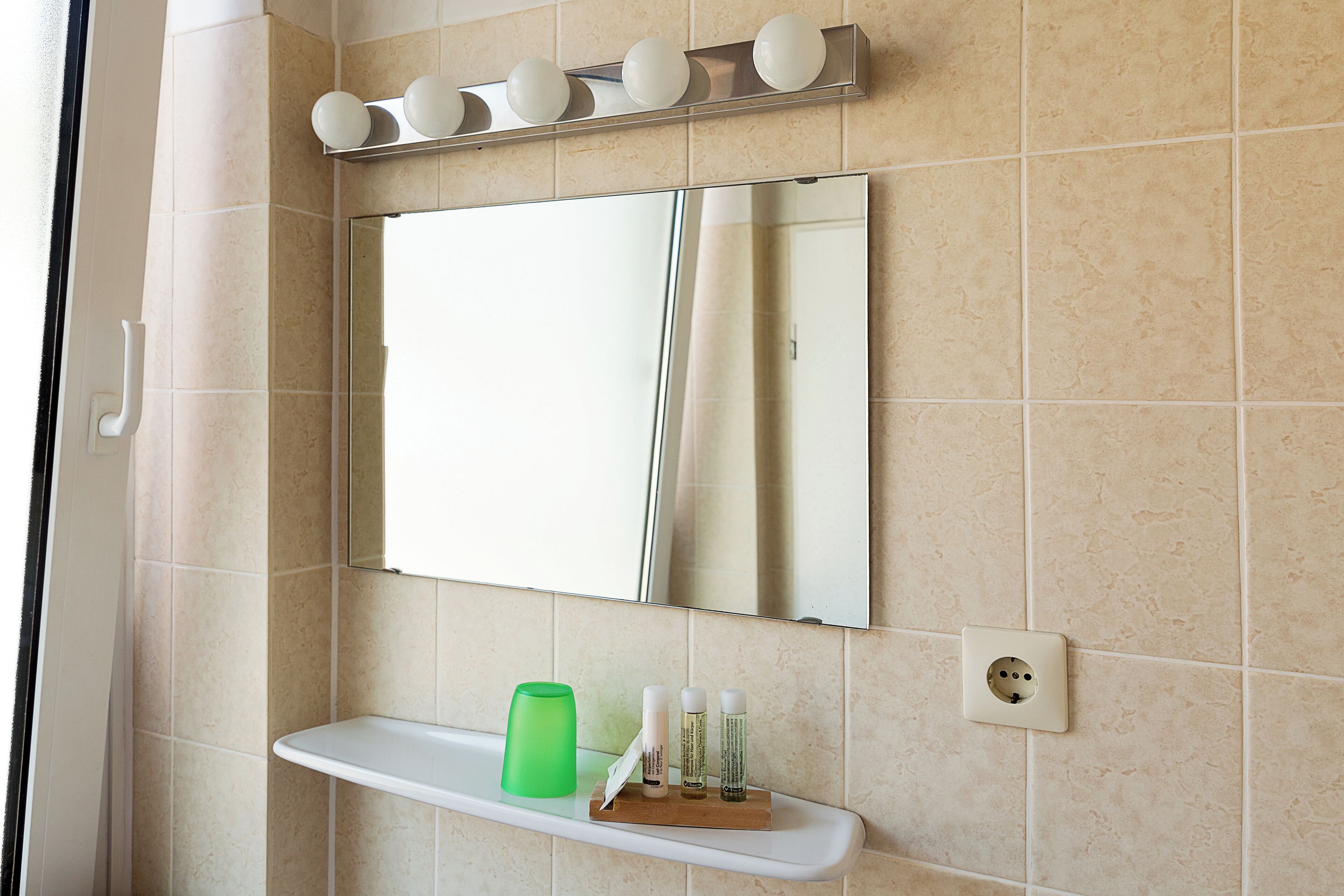 A bathroom with a mirror, a shelf with toiletries, and a light fixture.